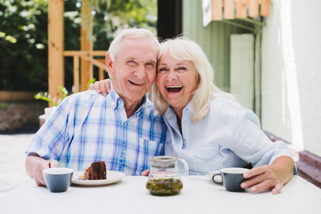 laughing elderly couple eating cake drinking tea